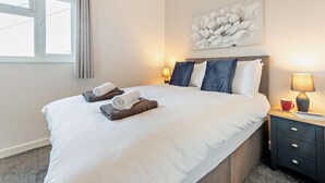 Ein Hotelzimmer mit einem großen Bett, zwei Nachttischlampen, einem Fenster mit Vorhängen und einem an der Wand hängenden Kunstwerk.
