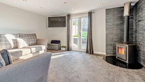 Ein modernes Wohnzimmer mit einem grauen Sofa, einem Flachbildfernseher, einem Kamin aus Stein und einer Schiebeglastür zum Garten.