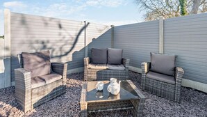 Eine Terrasse mit Korbmöbeln, einem Glastisch und einem weißen Teekessel.
