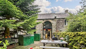A stone building with a green door, a picnic table, and a sandpit with toys. - 3 Bed in Skipton (oc-93485) (Embsay)