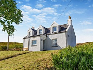 A two-story house with a gabled roof, a chimney, and a small front porch with a bench. - 2 Bed in Isle Of Skye (oc-93292) (Dunvegan)