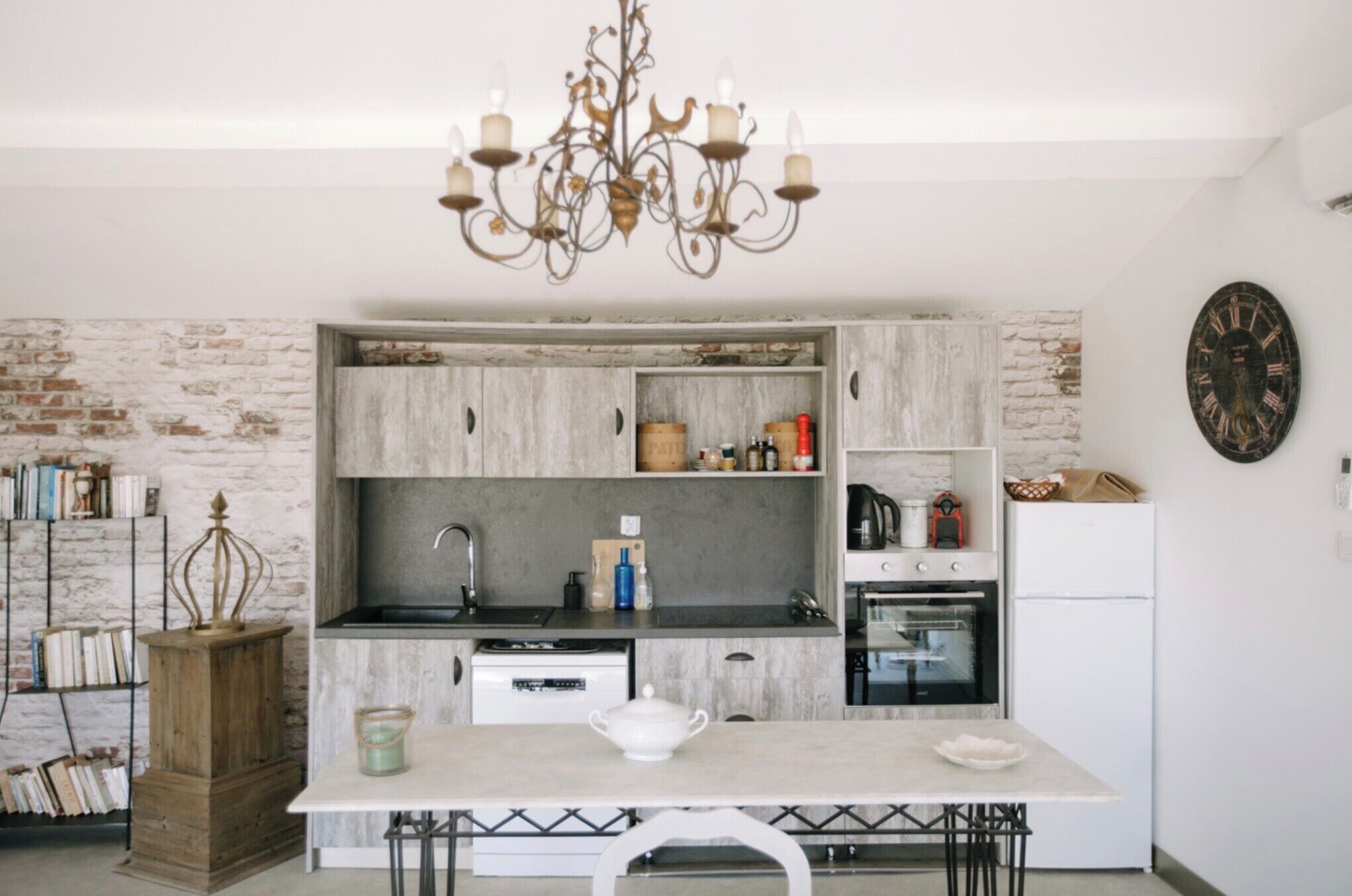 Une cuisine de taille modeste, avec un mur en briques au style rustique, un lustre et un réfrigérateur blanc.