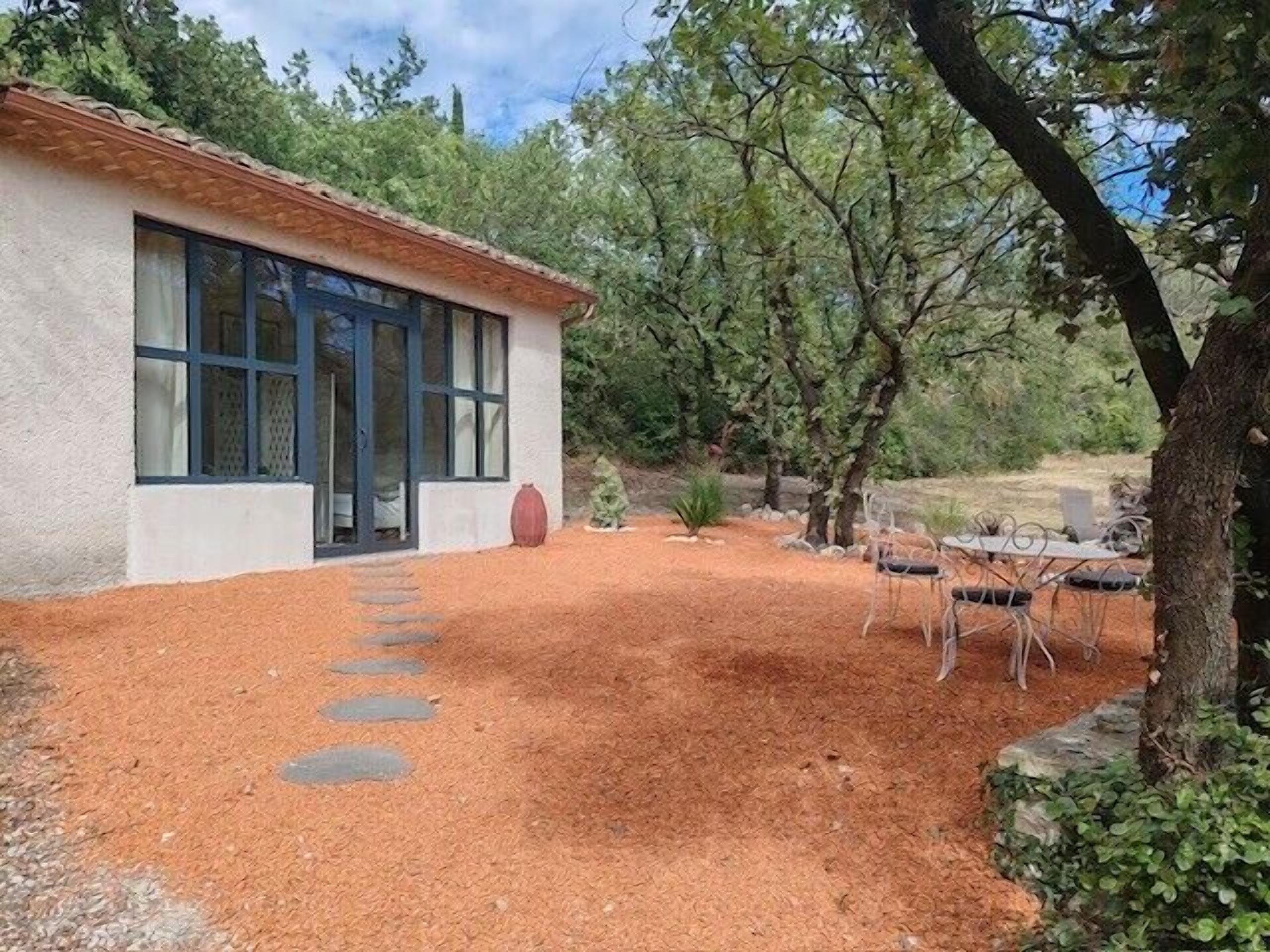 Un bâtiment à l’extérieur blanc, doté de grandes fenêtres, entouré d’un jardin avec un chemin de gravier menant à l’entrée.