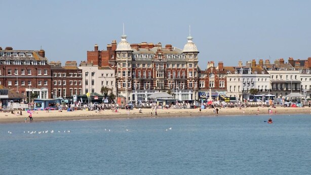 Un hôtel situé au bord de l’eau, de style architectural classique, avec plusieurs étages et un dôme imposant.