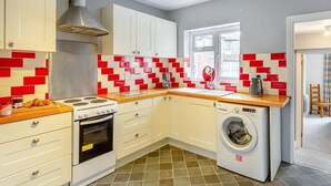 Une cuisine compacte avec des meubles blancs, une cuisinière, un four et un lave-linge.