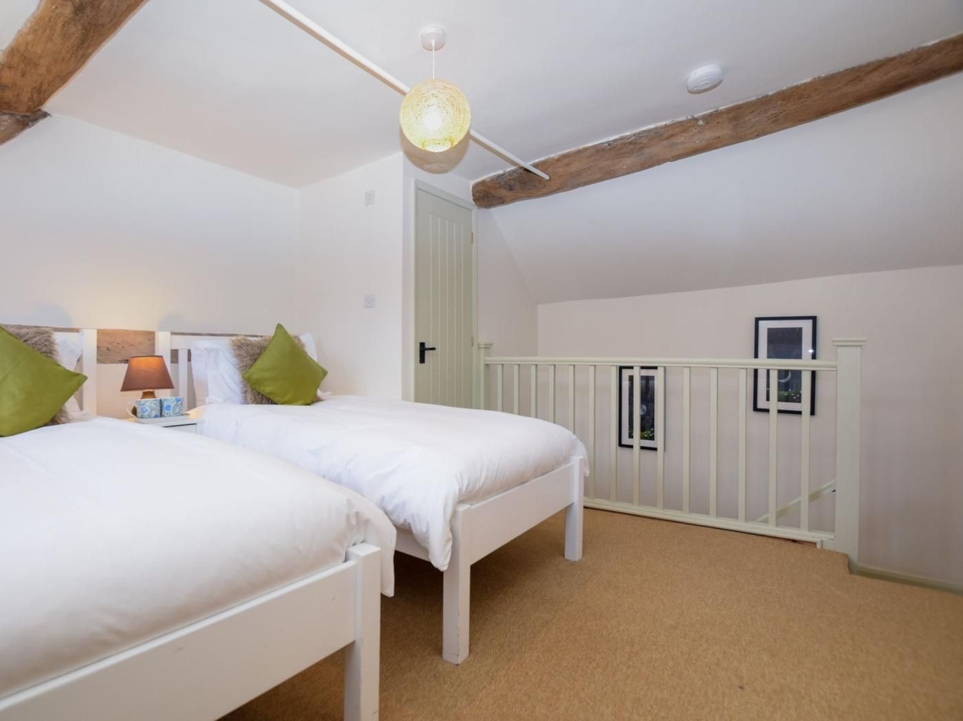 Ein Schlafzimmer mit zwei weißen Betten, einem Holzbalken an der Decke, einer Hängelampe und einer weißen Tür.