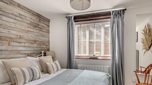 Un dormitorio con pared de madera, una cama con almohadas a rayas, una ventana con cortinas y un radiador.