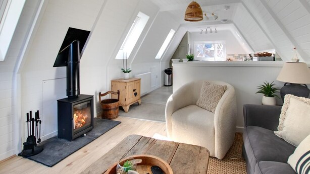 Habitación en el ático con chimenea, un sofá, una silla, un armario de madera y una zona de cocina.