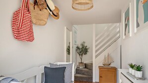 Un interior moderno con un sofá blanco, almohadones estampados, una silla colgante de mimbre, una mesita de noche de madera y una escalera.