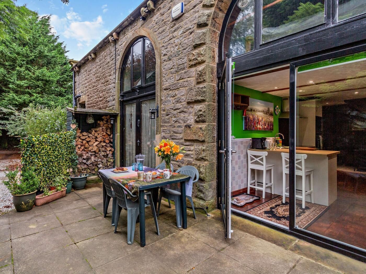 A stone building with a patio table and chairs, a green wall, and a kitchen area visible through the glass door.