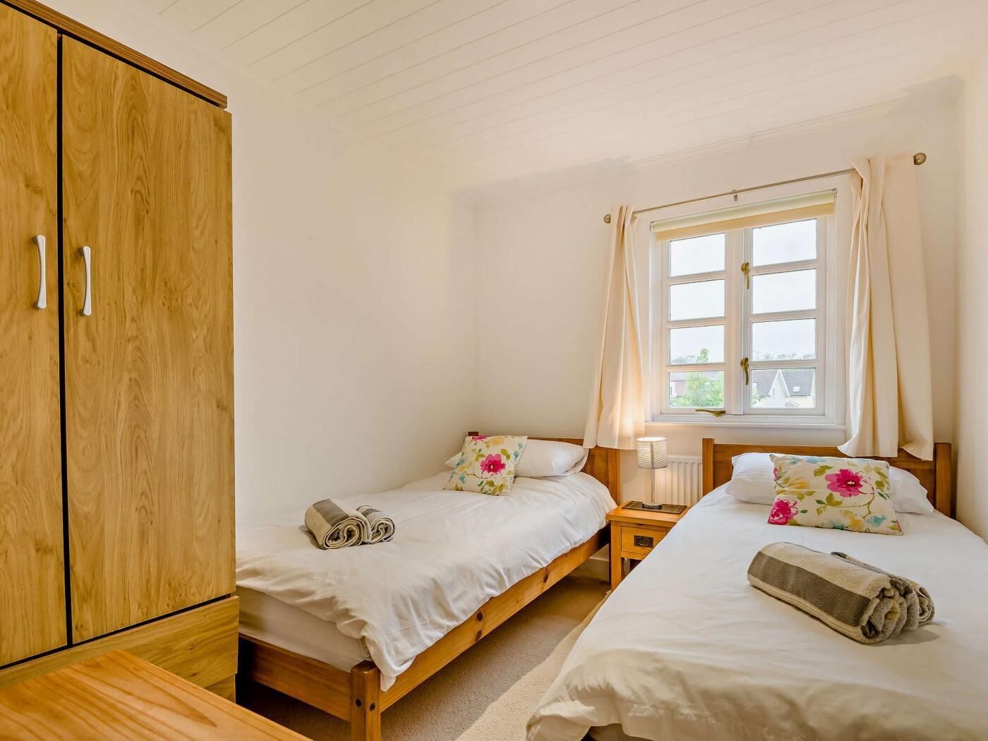 A bedroom with two single beds, a wooden wardrobe, a window with curtains, and a radiator.