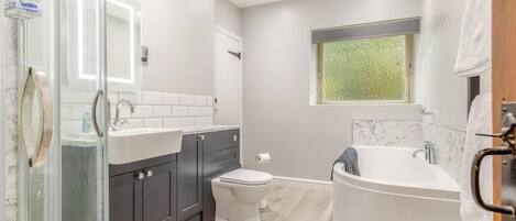 A modern bathroom with a glass shower enclosure, a white sink, dark cabinets, a toilet, and a freestanding bathtub.