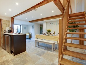Eine geräumige Küche mit Kochinsel, ein Essbereich mit Tisch für zwei Personen und eine Holztreppe.