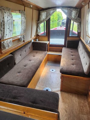 A compact interior with a sofa and bench seating, wooden flooring, and curtains.