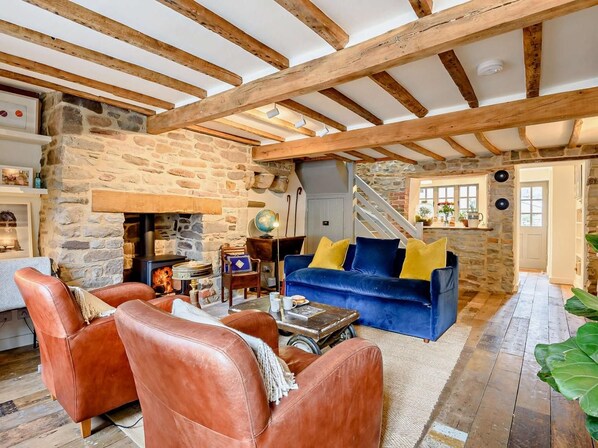 Ein rustikales Wohnzimmer mit freiliegenden Holzbalken, einem Steinofen, Ledersofas und einem blauen Sofa mit gelben Kissen.