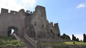 Un château historique en pierre, doté d’une grande entrée en arc de cercle, d’une tour centrale et d’un escalier menant à l’entrée principale.