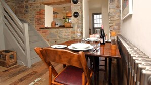 Un espace repas avec un mur en pierre, des poutres en bois, un escalier et un radiateur.
