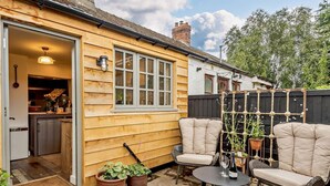 Une maison en bois avec une cuisine, deux chaises beiges, une petite table et des plantes en pot.