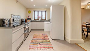 A modern kitchen with a central island, a dining area with a table and chairs, and a large window providing natural light. - 3 Bed in Penrith (oc-93379) (Orton)