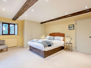 Ein Schlafzimmer mit Bett, Nachttisch, Lampe, Heizkörper, Fenster und Tür.