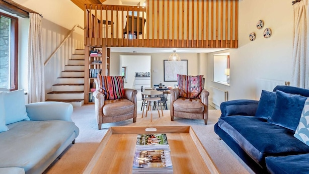 A spacious living area with a high ceiling, a staircase leading to an upper level, a dining area, and a sofa set. - 3 Bed in Penrith (oc-93379) (Orton)