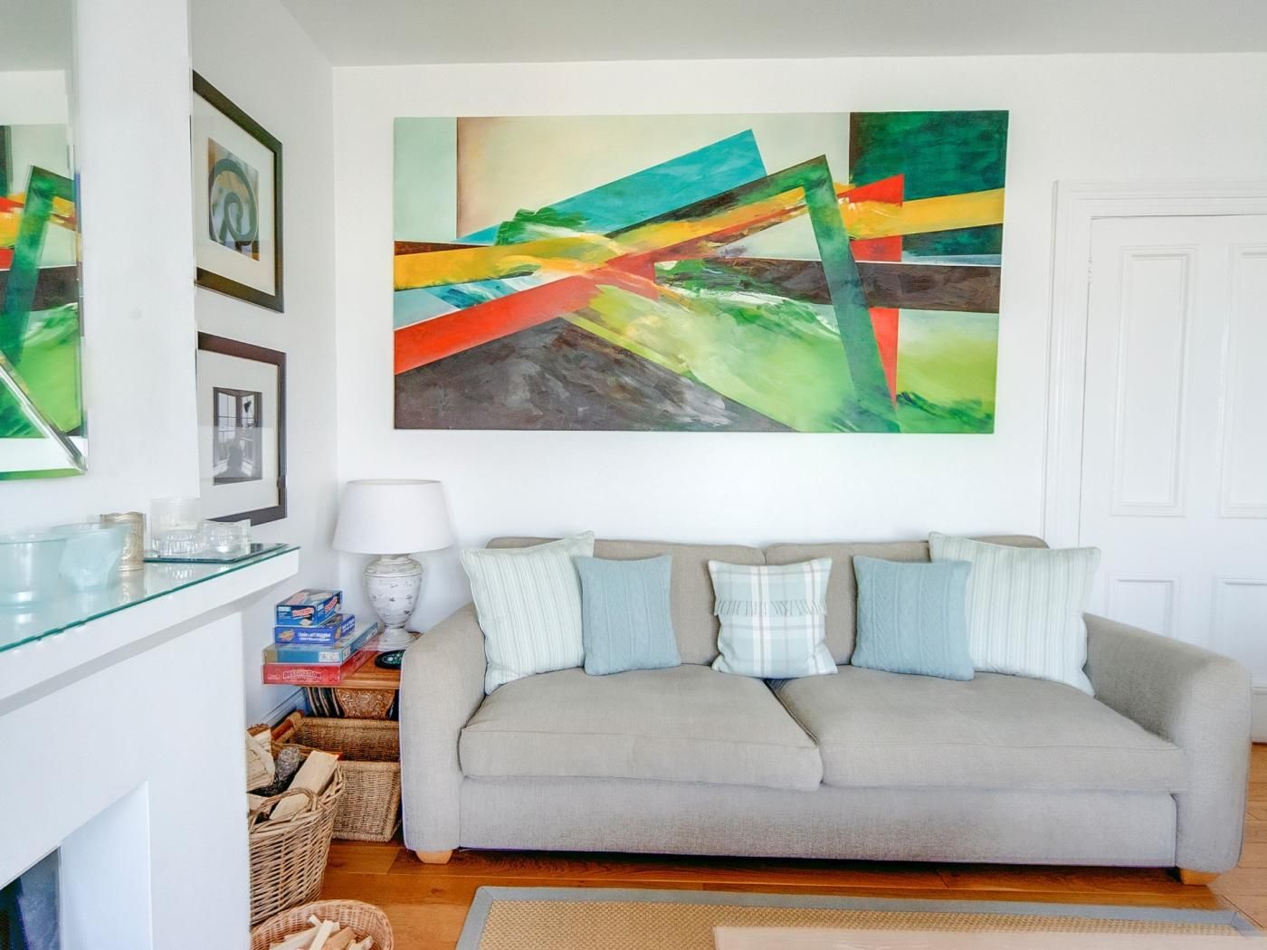 Una sala de estar con un sofá gris, una mesa de centro de vidrio y un cuadro abstracto colorido en la pared.