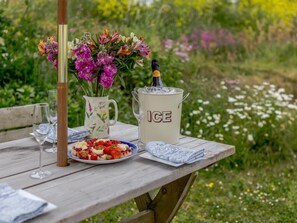 A picnic setup with a table, a floral vase, a bottle of champagne, a pitcher labeled 'ICE,' and a plate of strawberries. - 2 Bed in Helston (oc-54556) (Mullion)