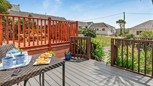 Een houten terras met een ontbijttafel, een omheind gebied en huizen op de achtergrond.