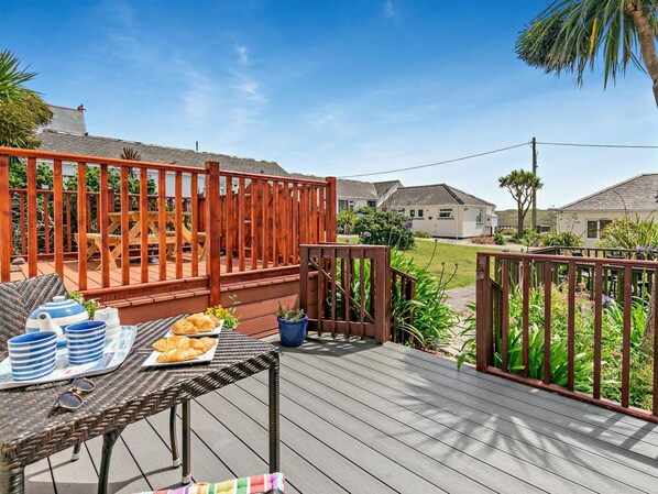 A wooden deck with a table set for breakfast, a fenced area, and houses in the background. - 2 Bed in Helston (oc-54556) (Mullion)