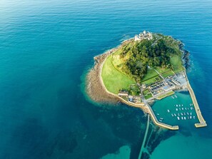 An aerial view of a coastal island with a castle, a marina with boats, and a well-maintained grassy area. - 2 Bed in Helston (oc-54556) (Mullion)