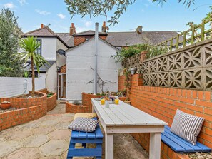 A patio area with a table and benches, surrounded by brick walls and a decorative fence. - 2 Bed in Weymouth (oc-94093) (Weymouth)