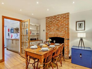 A dining area with a brick fireplace, wooden table, and chairs. - 2 Bed in Weymouth (oc-94093) (Weymouth)