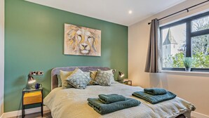 Ein Schlafzimmer mit einem Bett, Kunstwerken, Nachttischlampen, einem Fenster mit Vorhängen und Blick auf ein Gebäude.