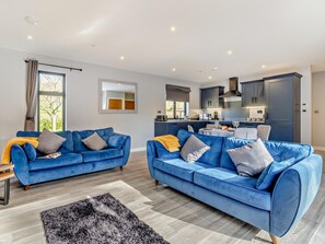 Een moderne woonkamer met twee blauwe banken, een zwart-wit vloerkleed en een keuken op de achtergrond.