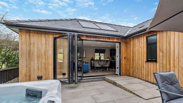 A modern outdoor patio with a hot tub, wooden walls, and a dining area visible through an open door. - 2 Bed in Knighton (oc-94202) (Knighton)