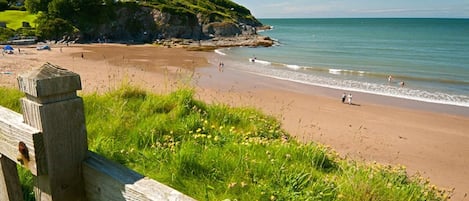 A coastal beach with a wooden fence in the foreground, a grassy area, and a clear sky.