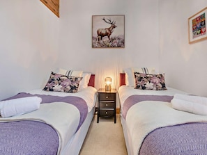 Habitación doble con dos camas, cada una con cubrecama estampado con motivos florales, una mesita de noche con lámpara y un cuadro enmarcado de un ciervo en la pared.
