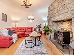 A cozy living room with a red leather sofa, a round wooden coffee table, a stone fireplace, and a chandelier. - 2 Bed in New Quay (oc-94160) (New Quay)