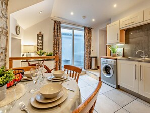 A modern kitchen with a washing machine, a dining area with a table set for four, and a view of the sea through large windows. - 2 Bed in New Quay (oc-94160) (New Quay)