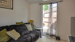 A living room with a sofa, pillows, a small table with a lamp, a TV, and a sliding door leading to an outdoor area. - 1 Bed in East Cowes (oc-91562) (Whippingham)