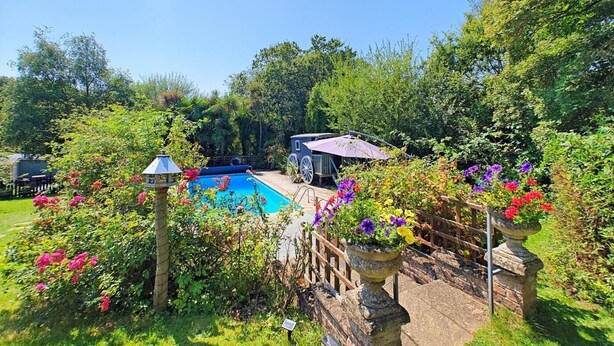A backyard with a swimming pool, a covered patio, and lush greenery. - 1 Bed in East Cowes (oc-91562) (Whippingham)