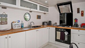 Une cuisine avec des meubles blancs, un plan de travail en bois, un évier, une cuisinière et une fenêtre.