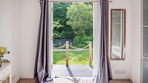 Une pièce avec vue sur un jardin et une rivière, un plancher en bois et un mur blanc avec une fenêtre.
