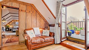 Ein Loft-Zimmer mit Holzbalkendecke, einem Ledersofa und einem großen Fenster mit Blick ins Freie.