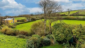 Un paisaje rural con una casa amarilla, campos verdes y cielo despejado.