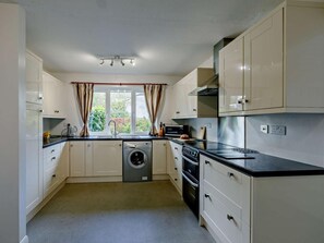 A compact kitchen with a washing machine, oven, and a window with curtains. - 2 Bed in Ilfracombe (oc-54106) (West Down)