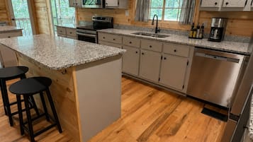 A kitchen with wooden cabinets, granite countertops, a stainless steel dishwasher, and a bar area with stools.