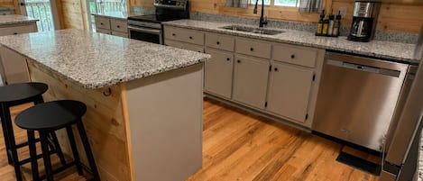 A kitchen with wooden cabinets, granite countertops, a stainless steel dishwasher, and a bar area with stools.