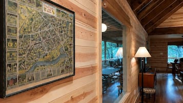 A wooden cabin interior with a large map on the wall, a dining area, and a view through a window.