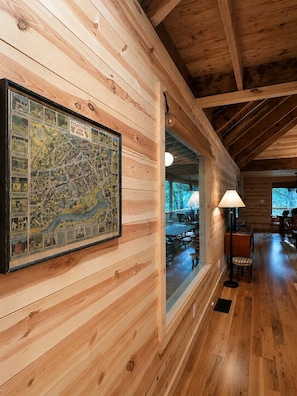 A wooden cabin interior with a large map on the wall, a dining area, and a view through a window.